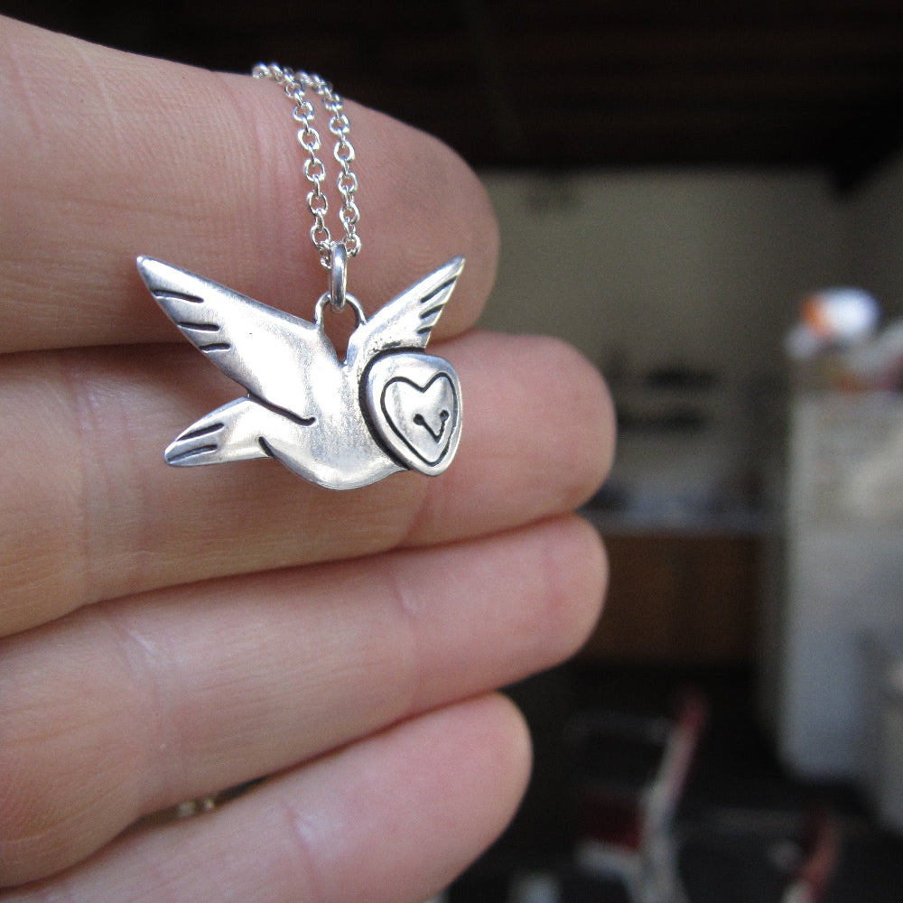 Silver barn owl pendant on a chain held in a hand.