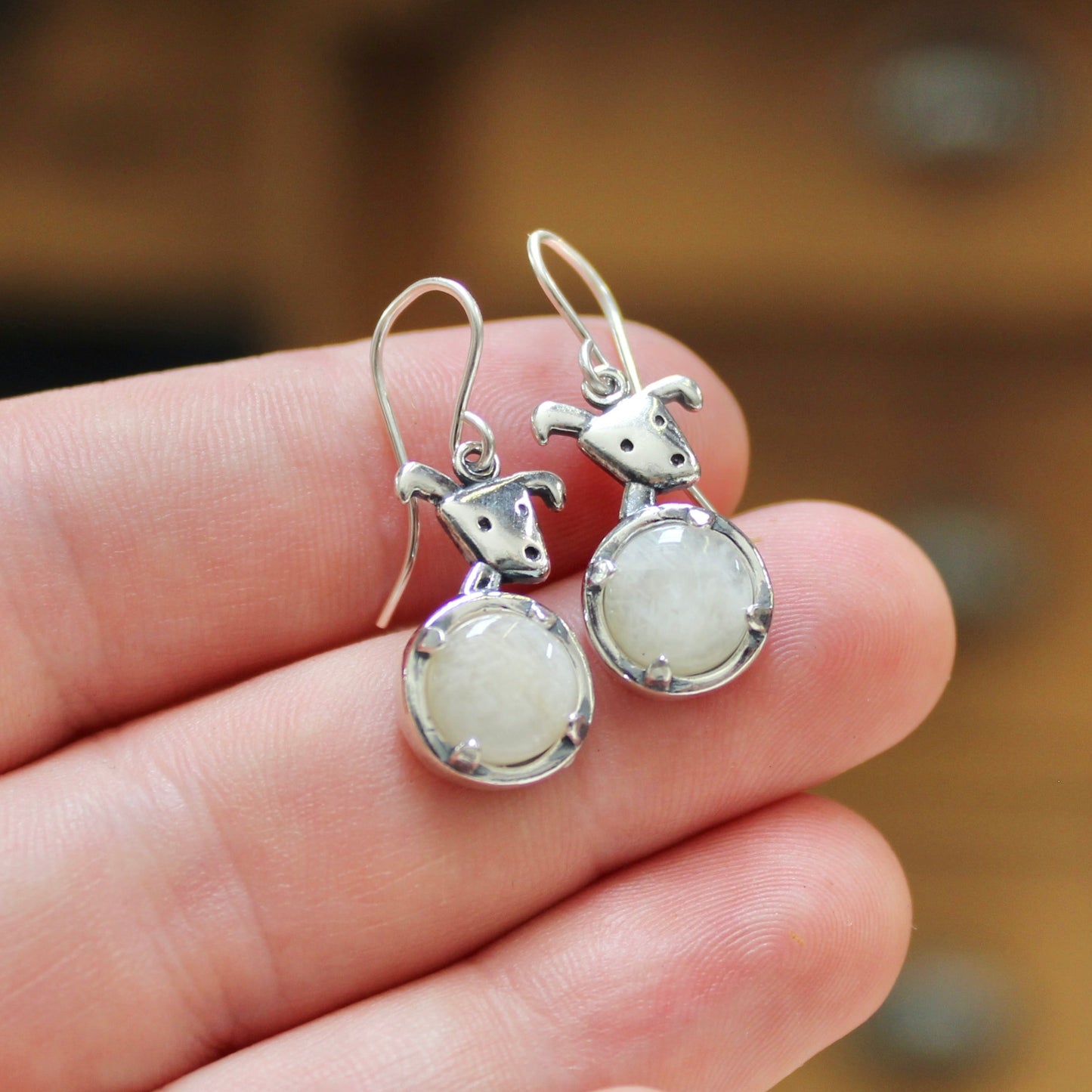 Silver earrings with white stones held in a hand against a blurred wooden background