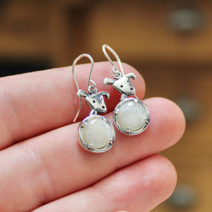 Silver earrings with white stones held in a hand against a blurred wooden background
