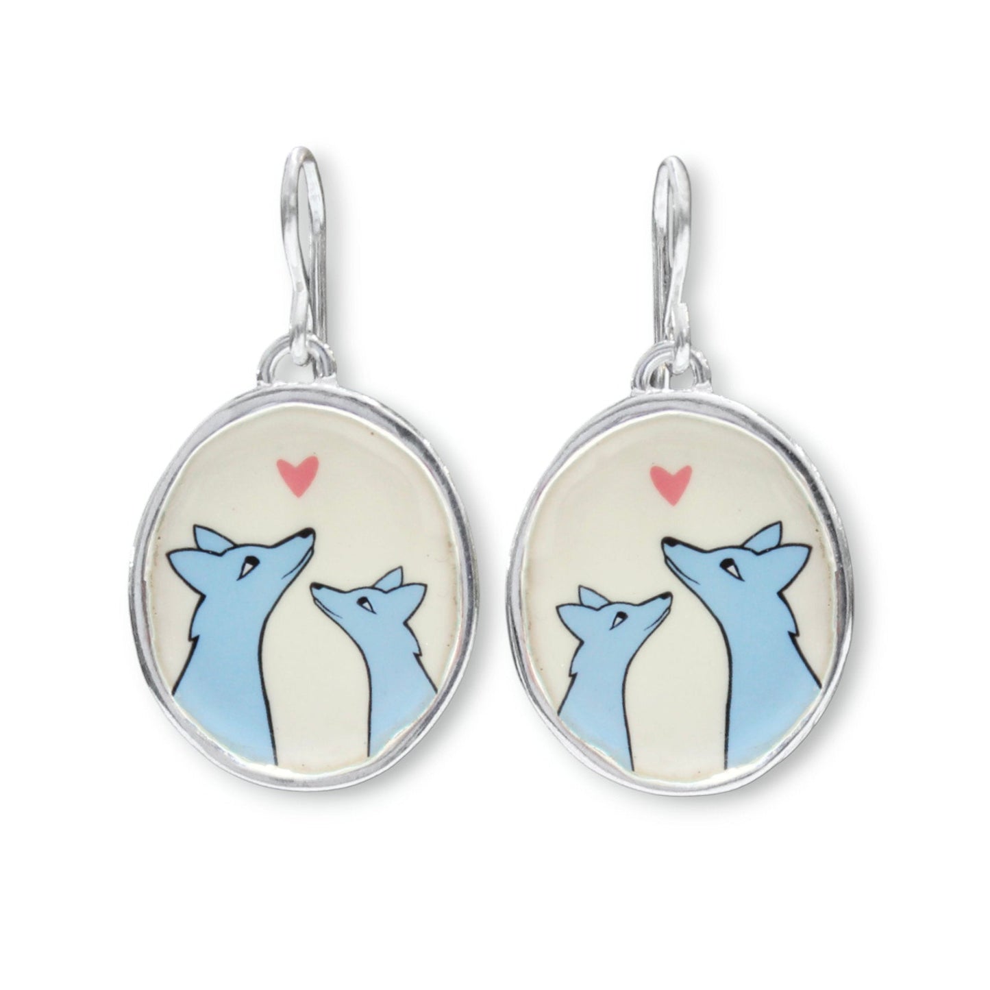 A pair of silver dangle earrings with oval charms featuring a cartoon illustration of two blue foxes looking at each other under a small pink heart on a cream background.