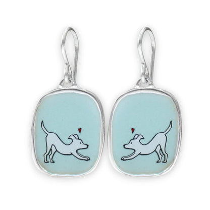 A pair of silver drop earrings with rounded rectangular bezel settings containing a light blue enamel background. Each earring features a white line-art illustration of a dog with a small red heart above it.