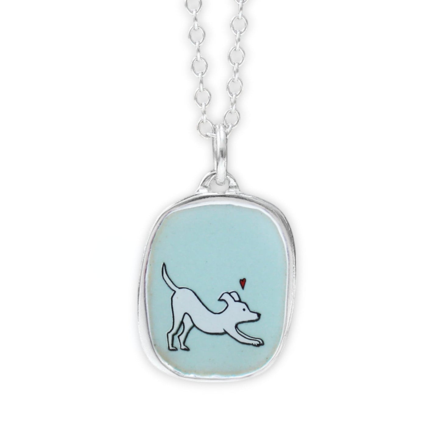 A silver pendant necklace featuring a light blue oval bezel with a white dog illustration and a small red heart, suspended from a silver chain on a white background.