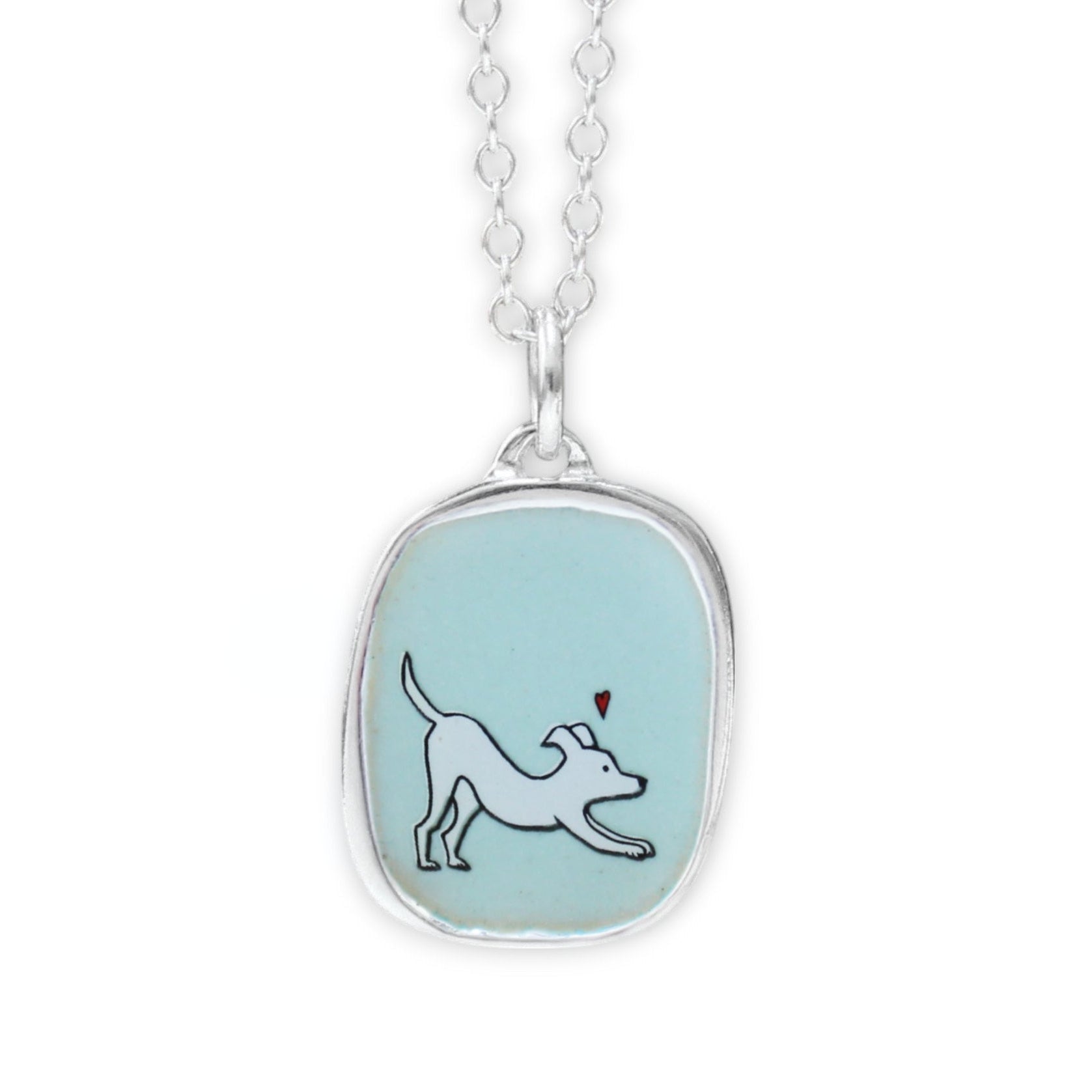 A silver pendant necklace featuring a light blue oval bezel with a white dog illustration and a small red heart, suspended from a silver chain on a white background.