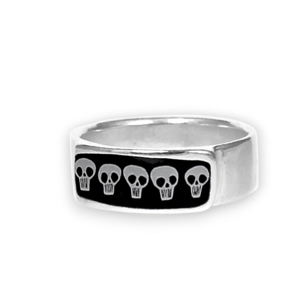 A silver-toned metal ring featuring a rectangular black inlay with five small white skull motifs, shown on a plain white background.
