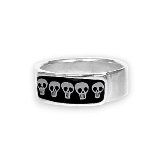 A silver-toned metal ring featuring a rectangular black inlay with five small white skull motifs, shown on a plain white background.